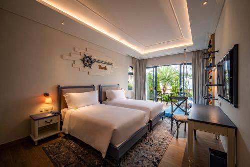 a hotel room with two beds and a desk and a window at Centara Mirage Resort Mui Ne in Mui Ne