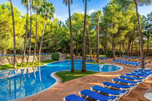 a resort pool with lounge chairs and palm trees at Valentin Grand Park Suite Hotel in Paguera