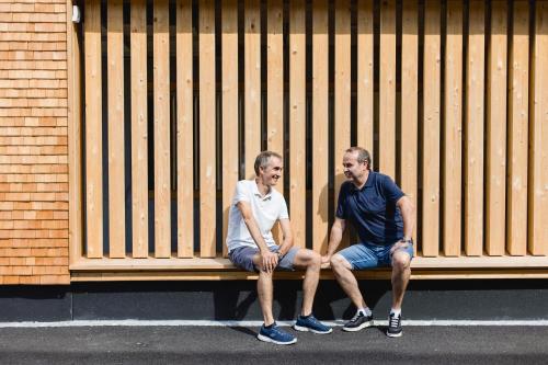 two men sitting on a bench in front of a building at am Greben Apartments eins - zwei - sechs - sieben in Bezau