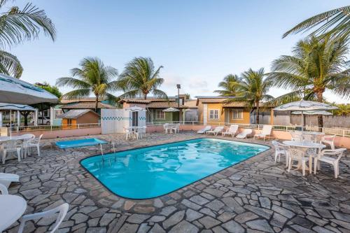 a swimming pool with tables and chairs and palm trees at Chalé Mares in Estância