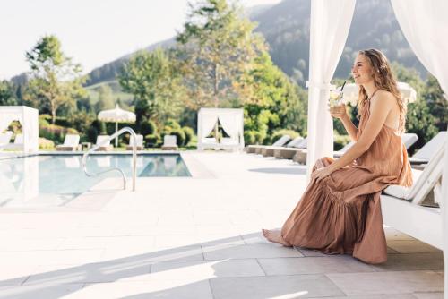 a woman sitting on a bench next to a pool at Alpenpalace Luxury Hideaway & Spa Retreat in Lutago