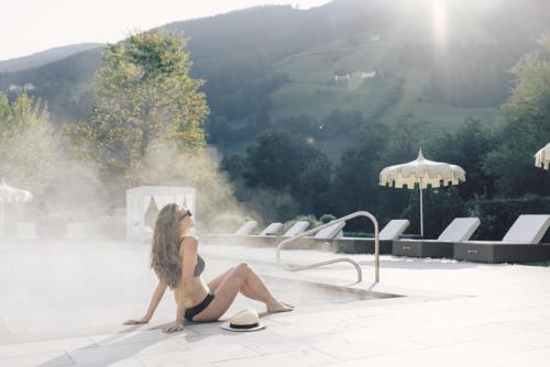 a woman in a bathing suit sitting next to a swimming pool at Alpenpalace Luxury Hideaway & Spa Retreat in Lutago