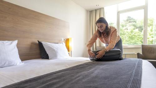 una mujer de pie en una cama con una maleta en Sanadome Hotel & Spa Nijmegen en Nijmegen