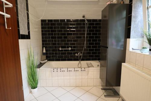 La salle de bains est pourvue d'une baignoire et d'un mur en carrelage noir. dans l'établissement Haus Flieder, à Krummhörn