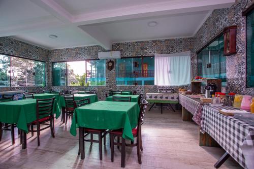 un restaurante con mesas verdes, sillas y ventanas en Pousada Guarubela Veloso, en Ilhabela