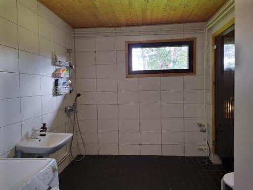 ein weiß gefliestes Bad mit einem Waschbecken und einem Fenster in der Unterkunft Holiday House Mäntyniemi in Hossa