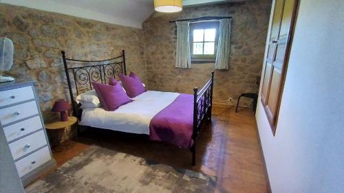 a bedroom with a bed with purple pillows on it at The Railway Cottage - characterful and comfortable holiday cottage in Piégut-Pluviers