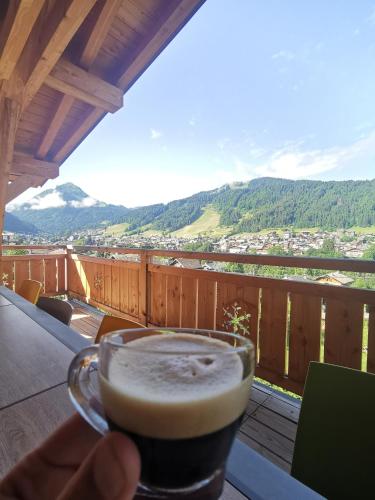 a hand holding a cup of coffee on a balcony at Résidence Julianna , trajets remontées mécaniques , livraison viennoiseries, piscine couverte in Morzine