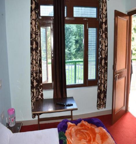 a room with a bed and a table and windows at Hotel Surat, Barot in Kasāmbal