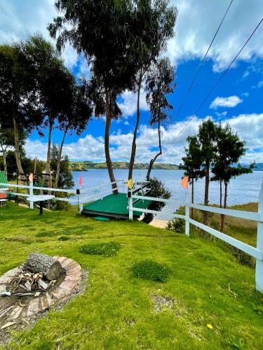 a grassy area with a boat on the water at La Puerta Del Lago ECOPARQUE in Tota