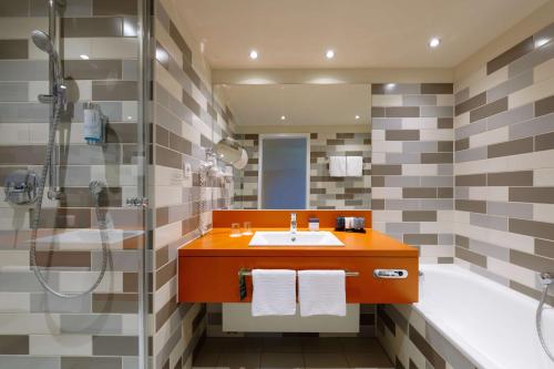 a bathroom with a sink and a shower and a tub at ATLANTIC Hotel Galopprennbahn in Bremen