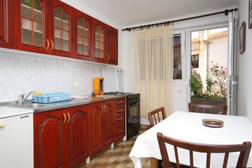 a kitchen with red cabinets and a table with a white tablecloth at Apartment Mali Losinj 7991b in Mali Lošinj