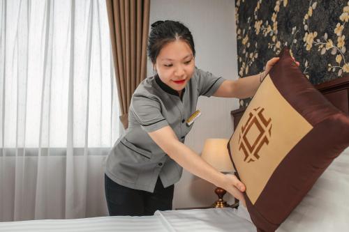 a woman putting a pillow on a bed at May De Ville Trendy Hotel & Spa in Hanoi