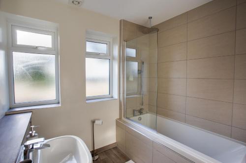 a bathroom with a tub and a sink and a bath tubermottermott at SAXON ROAD - A 3 Bedroom House with Garden by Prestigious Stays - Includes Wifi, Netflix & Amazon Alexa in Sunbury Common