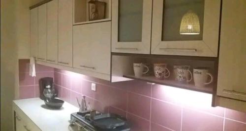 a kitchen with white cabinets and pink tile on the wall at Orea Kaliva in Sfinárion