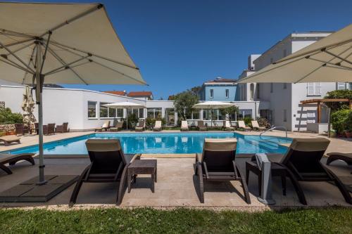 a pool with chairs and umbrellas next to a building at Hotel Manora in Nerezine