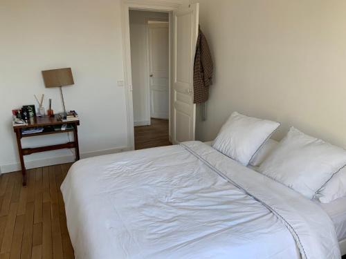 - une chambre avec un lit avec des draps blancs et une table dans l'établissement Appartement tout confort à 10 min de La Défense, à Colombes