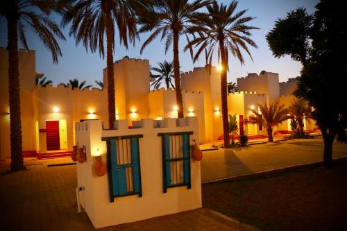 a white building with windows in front of palm trees at Coastline Resort in Mussanah
