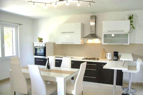 a white kitchen with a table and white chairs at Apartment Olivia in Šmrika