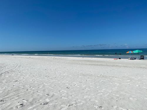 una playa de arena con dos sombrillas y el océano en Belleview Gulf Condos, en Clearwater Beach