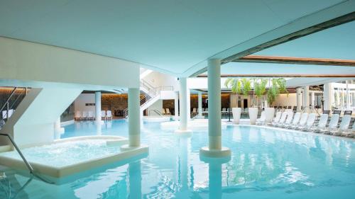 einen Pool mit weißen Stühlen in einem Gebäude in der Unterkunft Sanadome Hotel & Spa Nijmegen in Nijmegen