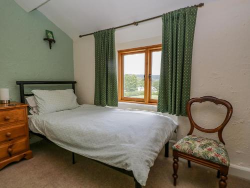 a bedroom with a bed and a window and a chair at 2 Gateside Cottages in Coniston