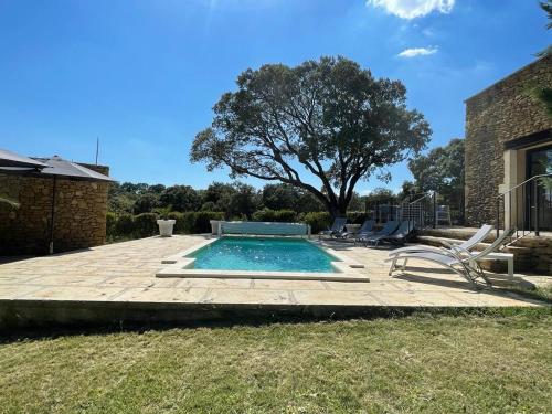 a swimming pool in a yard with chairs and a tree at Belle villa avec piscine intérieure et piscine extérieure Gite Les Aiguiers in Grignan