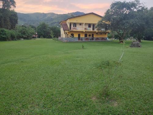 une maison jaune dans un champ avec une grande cour dans l'établissement Pousada Boa Vista, à Cachoeiras de Macacu