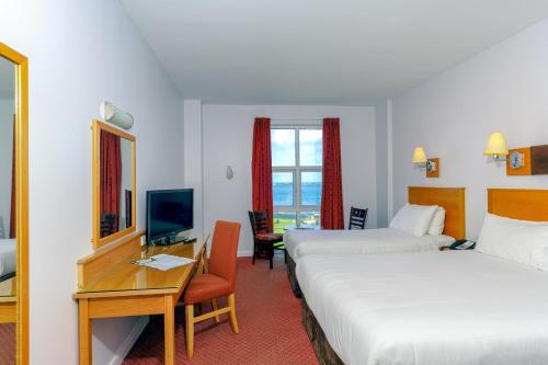 ポートラッシュにあるPortrush Atlantic Hotelのベッド2台、デスク、テレビが備わるホテルルームです。