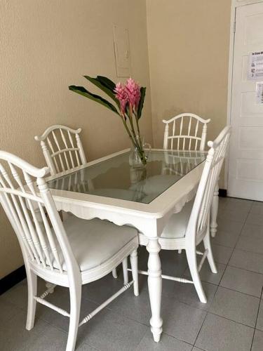 a glass table with three white chairs and a vase with flowers at Lush Tropical apartment located in a 4-star resort in Runaway Bay