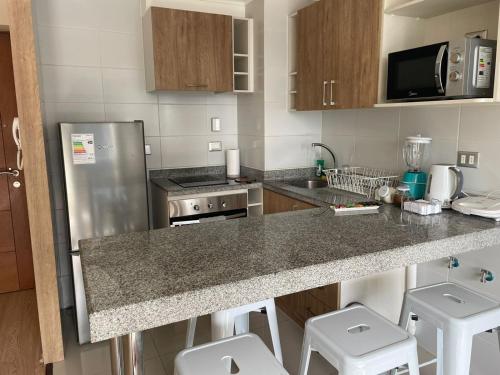 a kitchen with a stainless steel refrigerator and white stools at Departamento Chillan céntrico in Chillán