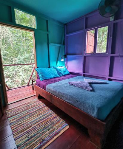a bedroom with a bed with purple walls and windows at Hidden Jungle Beach House in Puerto Viejo