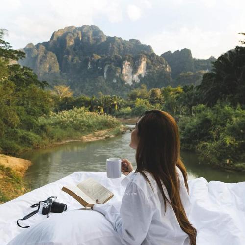 a woman sitting at a table with a book and a cup of coffee at Phu Siab Mhok@KhaoSok in Khao Sok