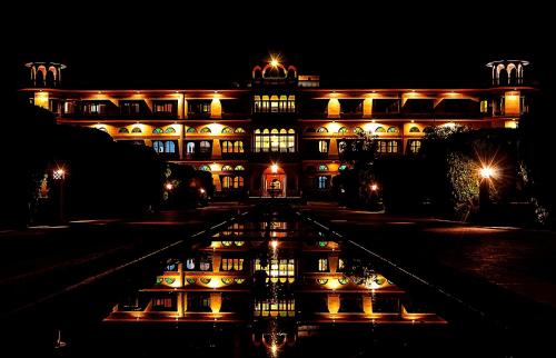 a building lit up at night with a reflection in the water at Umaid Palace - A Lakeside Resort - 25 minutes from Mehandipur Balaji - 20 minutes from Chand Baori Stepwell Abhaneri & 40 minutes from Bhangarh Fort in Dubbī
