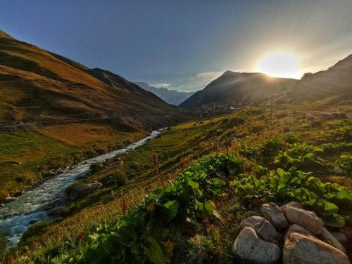 a river in a field with the sun setting in the background at Vila Latphari in Ushguli in Ushguli