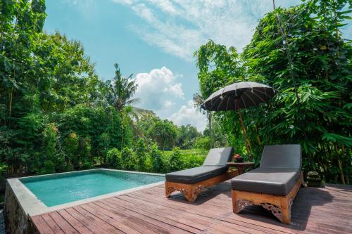 a patio with two chairs and an umbrella and a pool at KajaNe Yangloni at Ubud Bali in Ubud