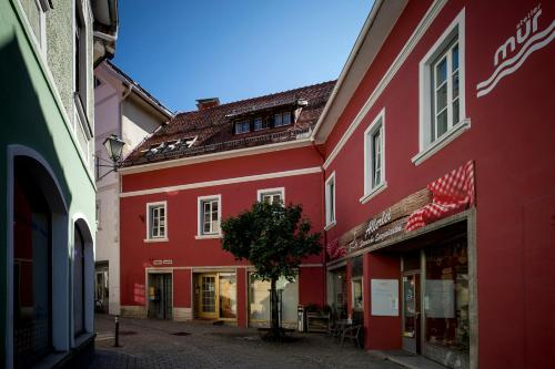 a red building with a tree in a street at Studio Loft Murau - im Herzen der Altstadt in Murau