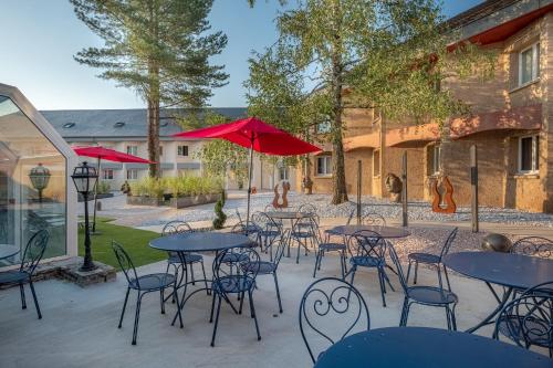 a patio with tables and chairs and red umbrellas at Hôtel Causse Comtal Rodez, The Originals Relais in Gages-le-Haut