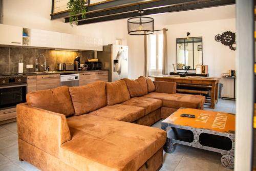 een woonkamer met een bruine bank en een keuken bij Loft 90 m2 cosy au calme avec terrasse et parking in Avignon