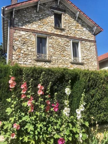 ein Steingebäude mit Fenstern und einer Hecke mit Blumen in der Unterkunft Home Sweet Home in Baillet-en-France