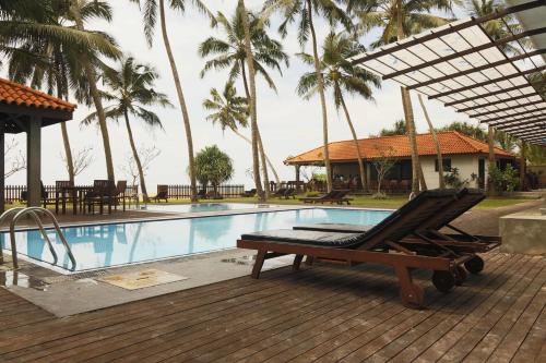 a lounge chair next to a swimming pool with palm trees at Blue Beach Hotel in Wadduwa