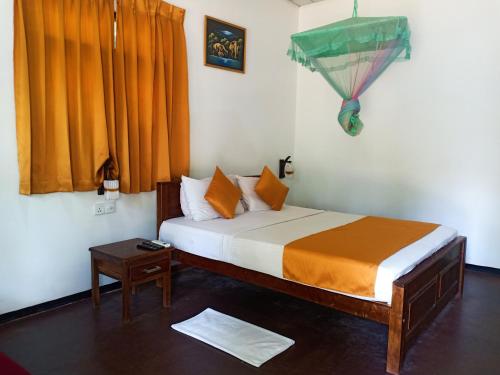 a bedroom with a bed with orange curtains and a table at Green View Safari Resort in Udawalawe