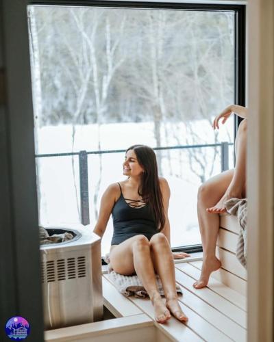 a woman sitting on a window sill looking outside at Chalet Flodhaus- Bord Rivière St-Maurice (navigable) / SPA /SAUNA - Chalets Galaxia in Saint Roch de Mekinac