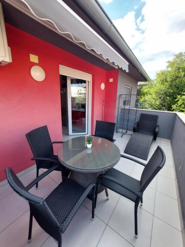 um pátio com uma mesa e cadeiras e uma parede vermelha em Apartman Noa em Jadrija