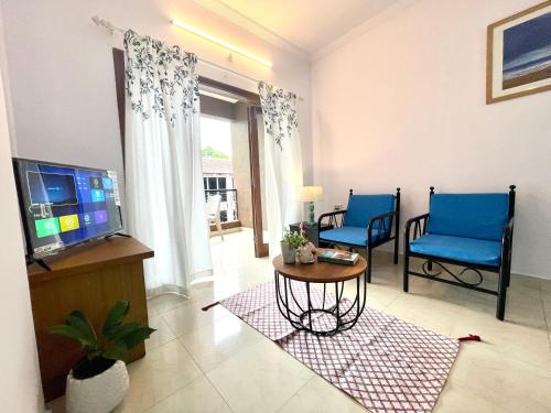 a living room with two blue chairs and a television at Sun-kissed Holidays, Goa Topaz in Candolim