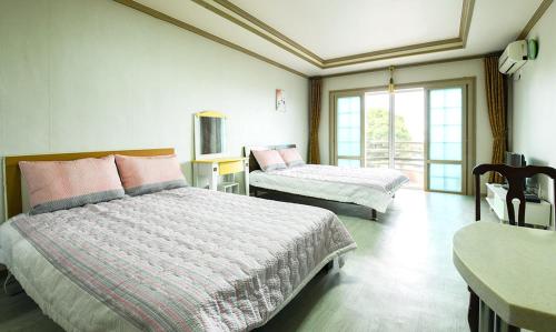 a bedroom with two beds and a table and a window at Yeonhwachon Pension in Jeju