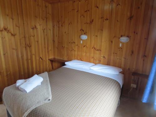a bedroom with a bed with wooden walls and white sheets at Captain Cook Holiday Park in Adventure Bay