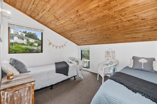 a bedroom with two beds and a wooden ceiling at The Family Bach - Cable Bay Holiday Home in Cable Bay