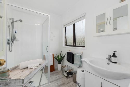 a white bathroom with a sink and a mirror at The Family Bach - Cable Bay Holiday Home in Cable Bay