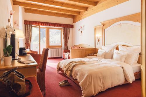 a hotel room with a bed and a desk and a desk at Wellness Refugium & Resort Hotel Alpin Royal - Small Luxury Hotels of the World in Cadipietra